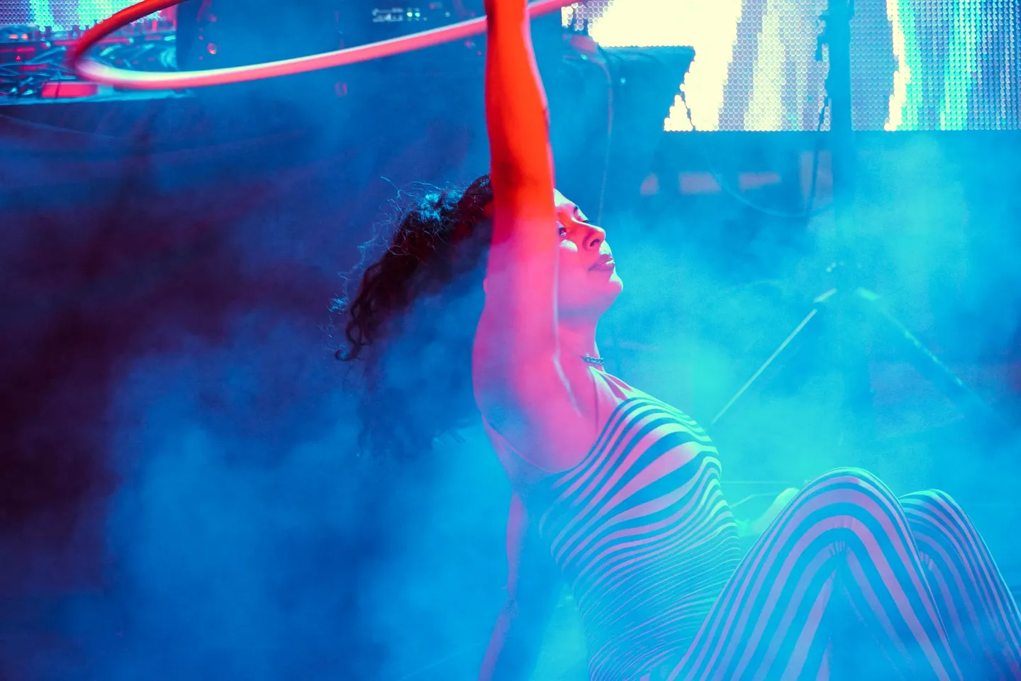 Artista de hula hoop con maillot de rayas girando un aro entre humo azul