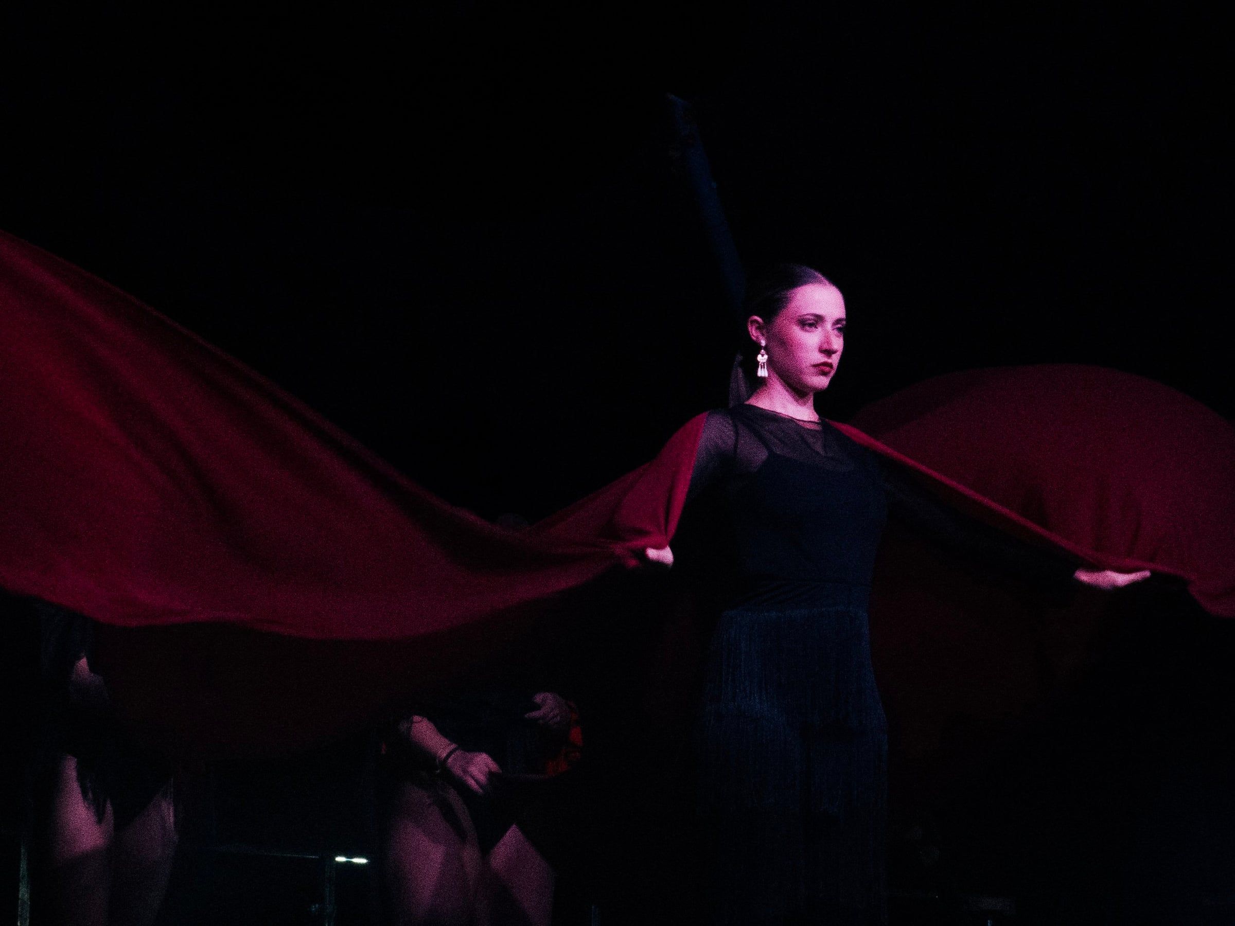 Bailaora de flamenco sobre un escenario oscuro sosteniendo una gran tela roja que ondea a ambos lados